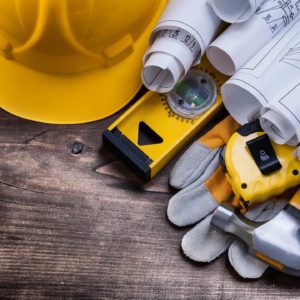 A yellow hard hat, tools and blueprints on a wooden table.