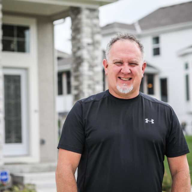 A man smiling in front of a house.