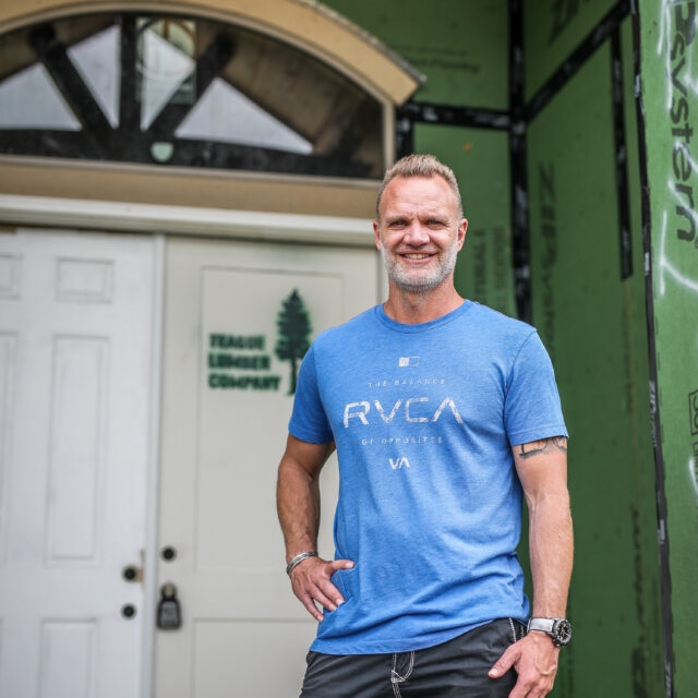 A man in a blue t-shirt standing in front of a house.