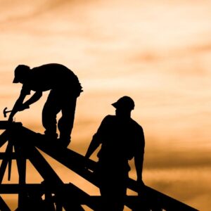 Two construction workers working on a roof at sunset.